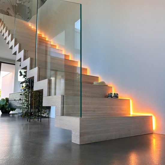 Moderne Faltwektreppe mit LED-Beleuchtung an der Wand, mit eingelassenem Glasgeländer, installiert in einem Haus mit Betonboden