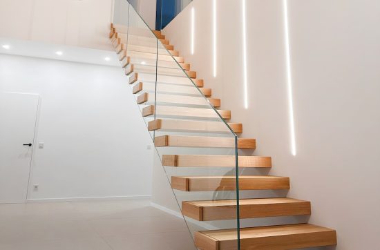 Eine moderne Kragarmtreppe mit Glasgeländer in einem weißen Treppenhaus an einer Wand mit LED-Beleuchtung.