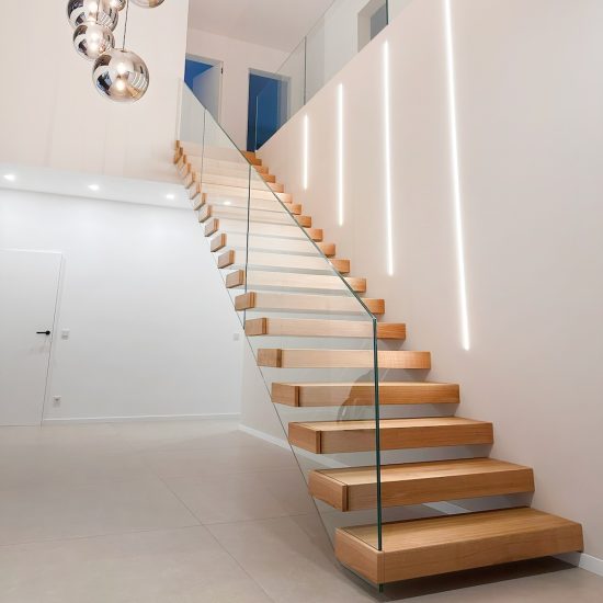 Eine moderne Kragarmtreppe mit Glasgeländer in einem weißen Treppenhaus an einer Wand mit LED-Beleuchtung.